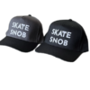 SKATE SNOB Branded Baseball Caps (Snapbacks) One is black with white raised embroidery. The other is grey/black bib with white raised embroidery.